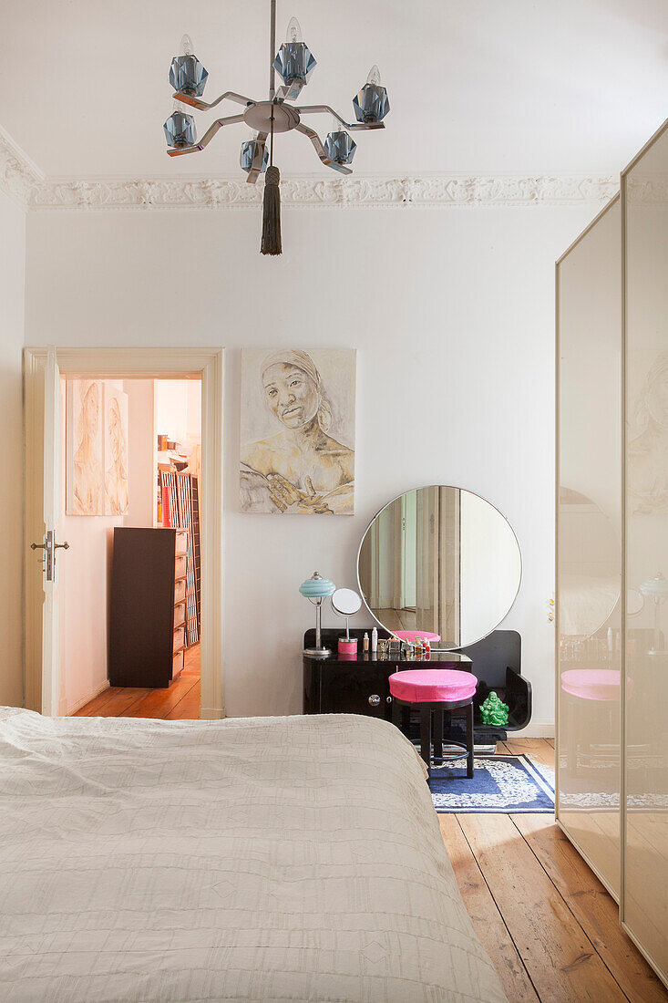 Doppelbett und weißer Kleiderschrank im Schlafzimmer, im Hintergrund schwarzer Schminktisch und rosa Hocker