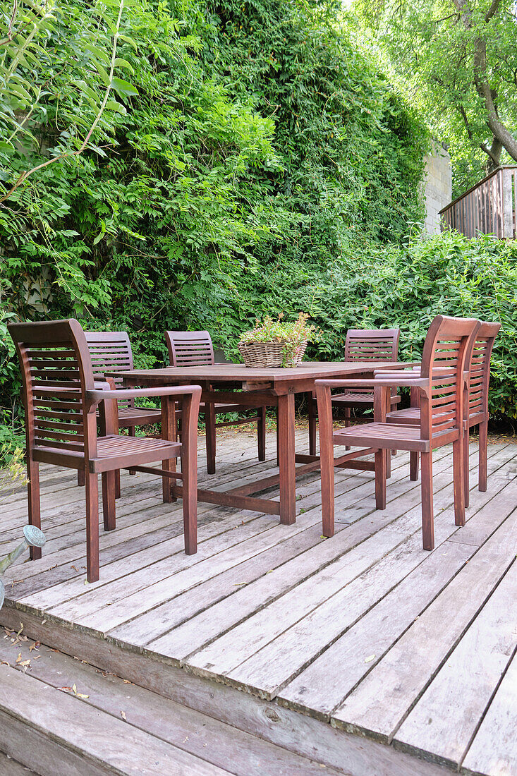 Wooden table and chairs on terrace with green hedge in the background