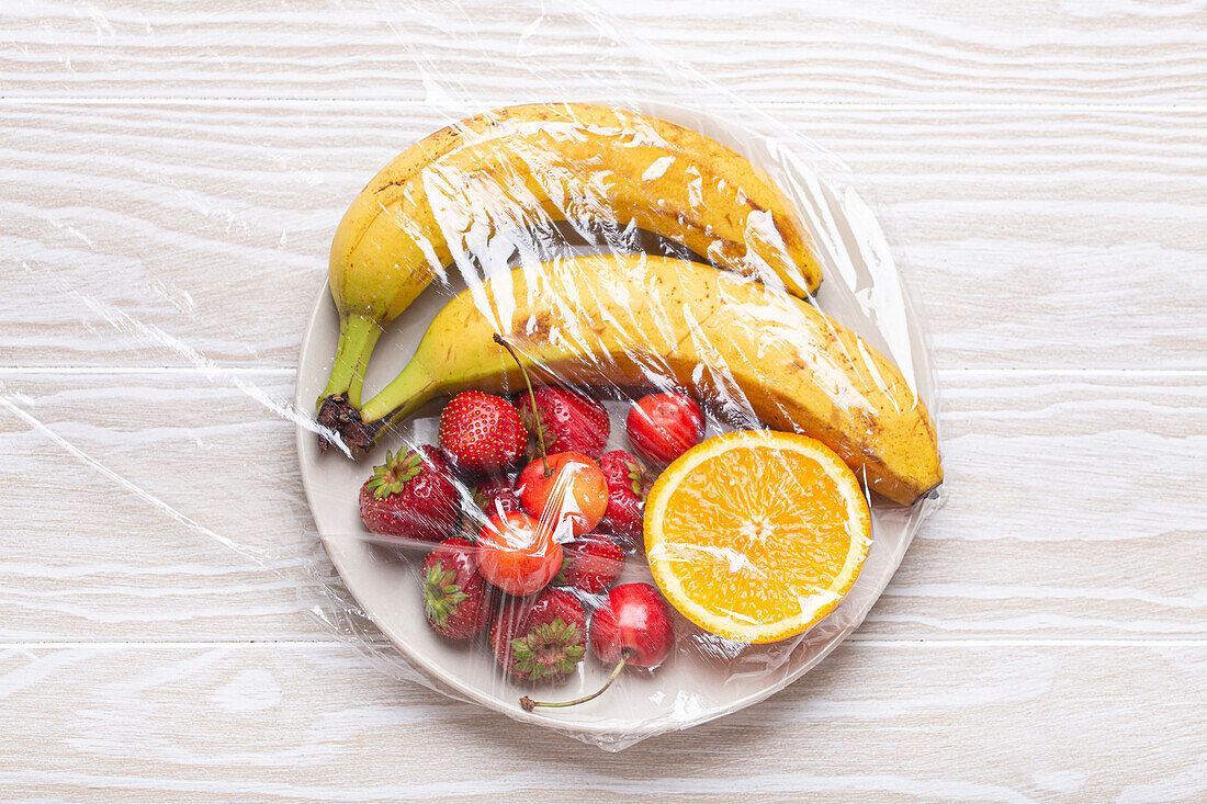Fruit and berries on a plate under plastic wrap