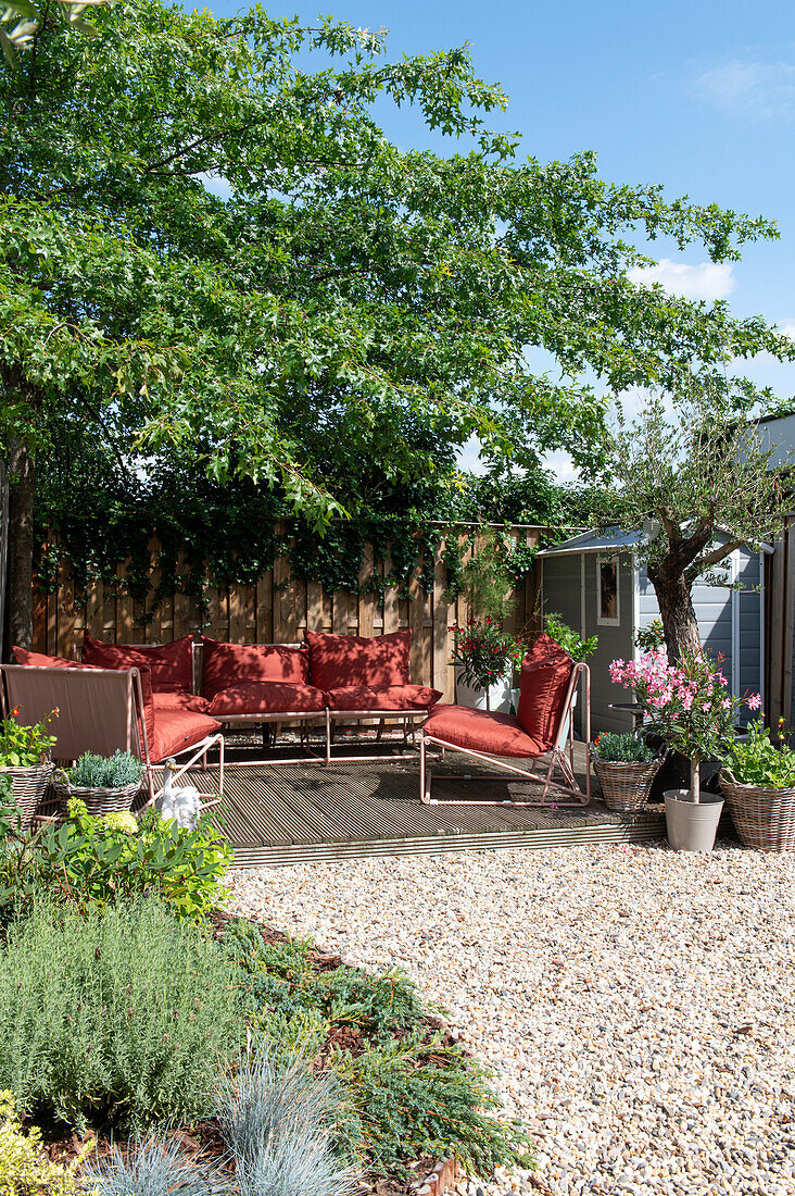 Terrasse mit roten Loungemöbeln und Topfpflanzen im Sommergarten