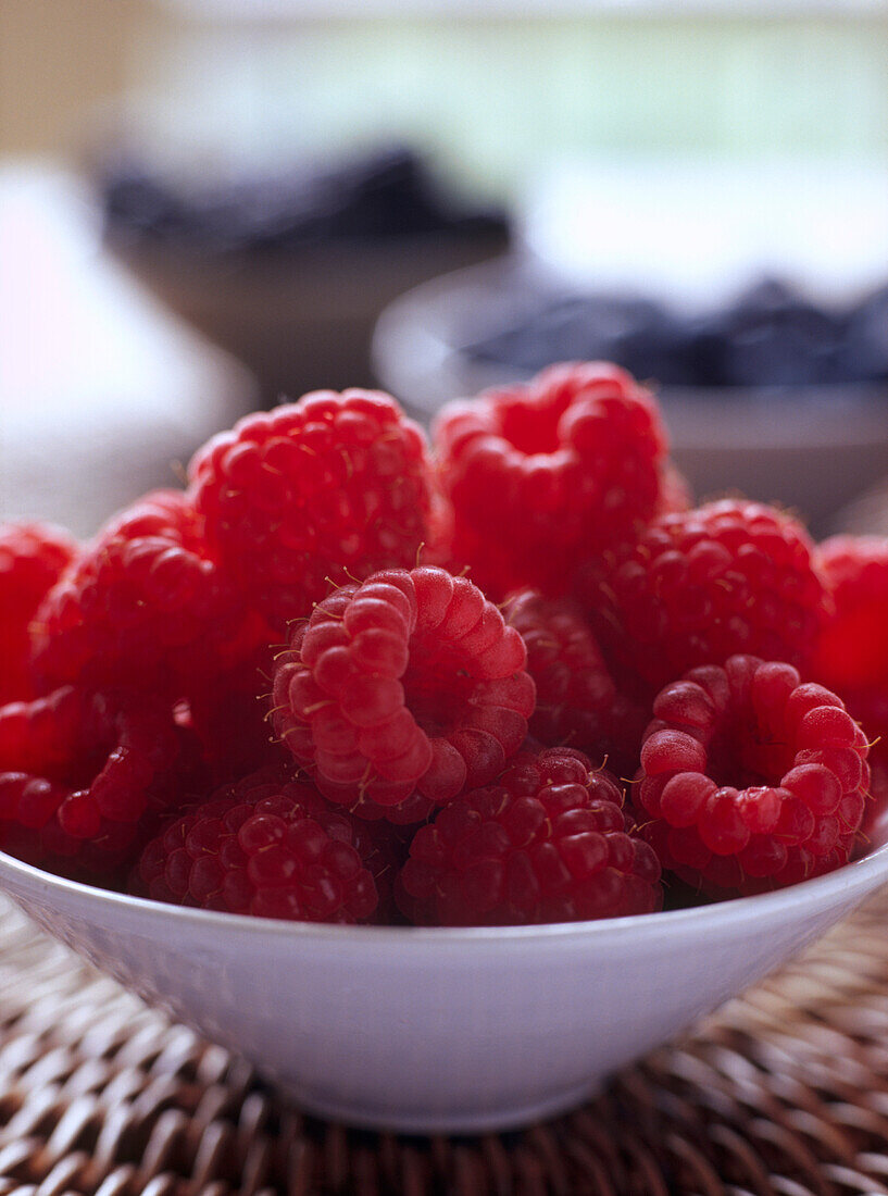 Schale mit frischen Himbeeren und Blaubeeren im Hintergrund