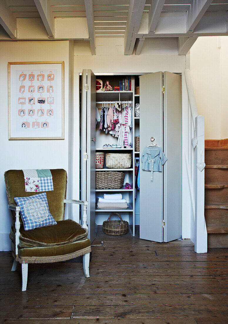 Childs clothing in storage cupboard with velvet covered armchair in Brighton home East Sussex, England, UK