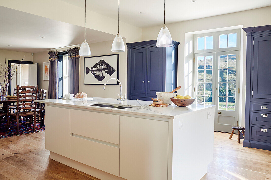 Blue painted storage and island unit with wooden floor in North Yorkshire farmhouse kitchen, UK