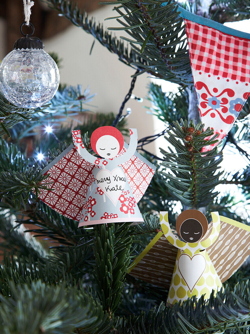 Paper angels and glass bauble with bunting in Christmas tree of Herefordshire cottage, England, UK