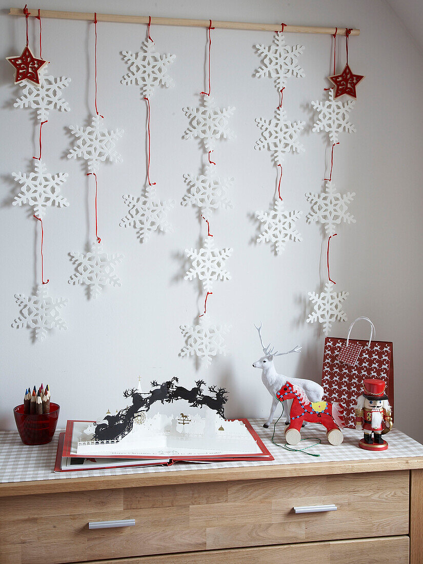 Schneeflocken-Wanddekoration und Pop-up-Weihnachtsbuch auf einer Kommode in einem Familienhaus, Polen