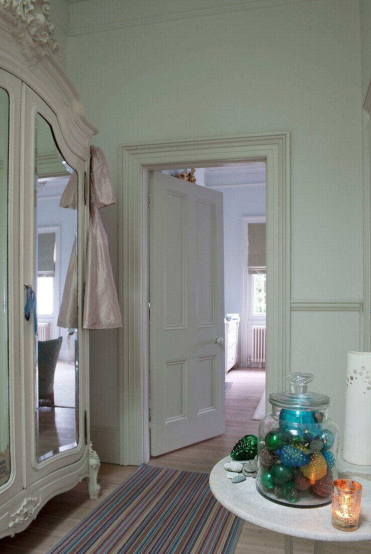 View from landing into bedroom with large mirrored ornate wardrobe and marble tabletop with a jar of baubles