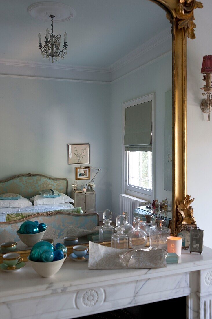 Marble fireplace with large gilt mirror reflecting the bedroom with ornate silk upholstered bed