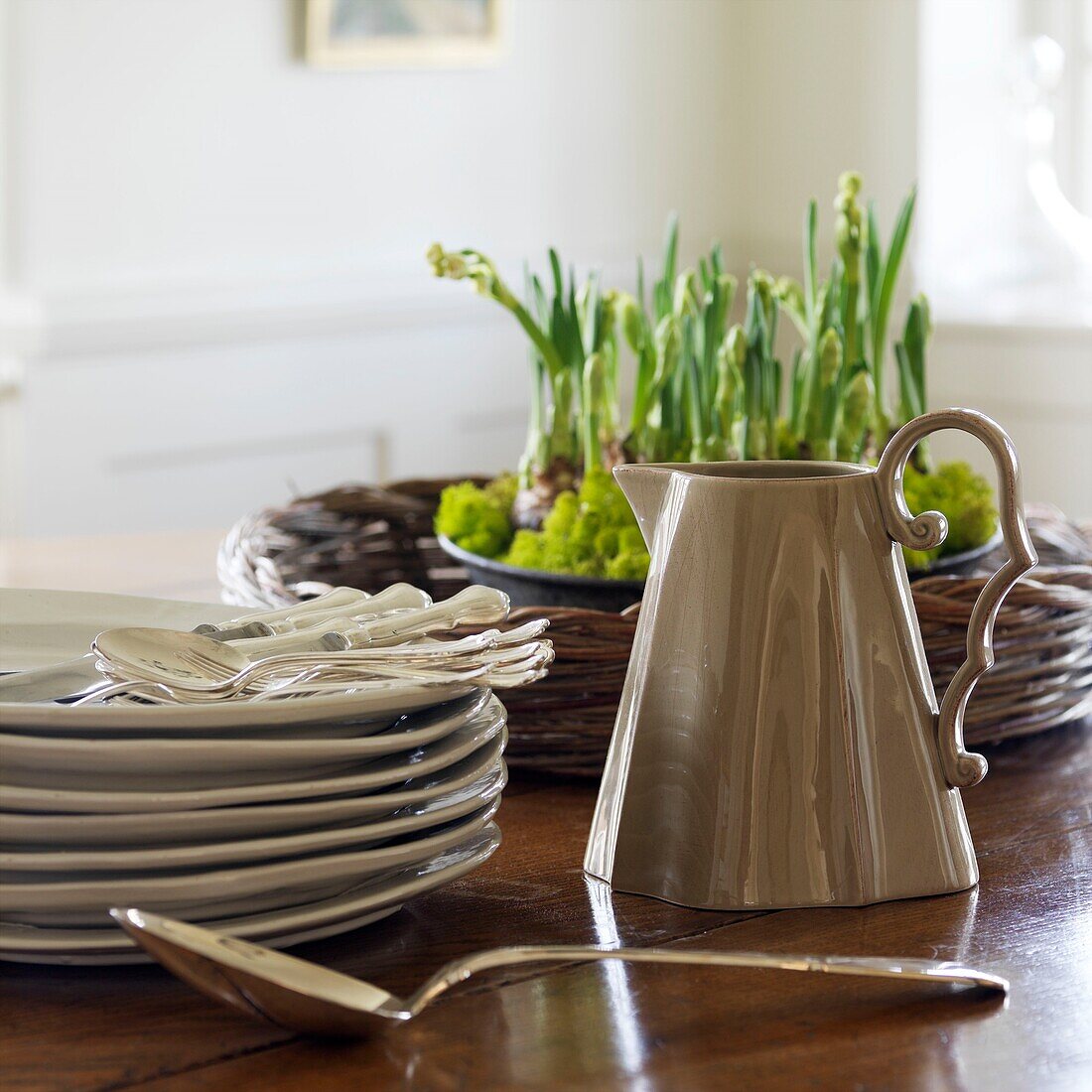 Tellerstapel, Krug und Frühlingsblumen auf einem Tisch