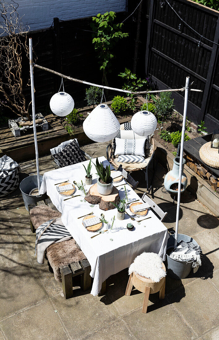 Solarlaternen über dem Tisch mit Sitzgelegenheiten aus Holz und Kissenstoffen auf der Terrasse in Colchester, Essex, UK