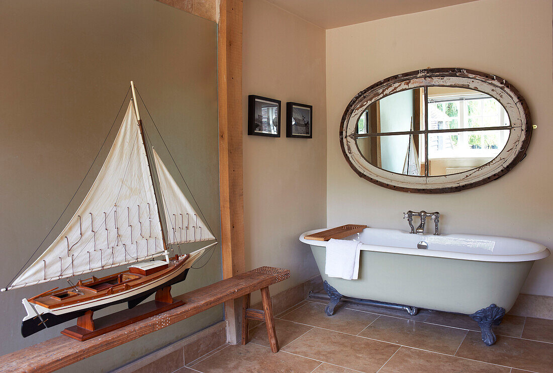 Freistehende Badewanne und Modellboot mit geborgenem Spiegel in einem Bauernhaus in Iden, Rye, East Sussex, Vereinigtes Königreich