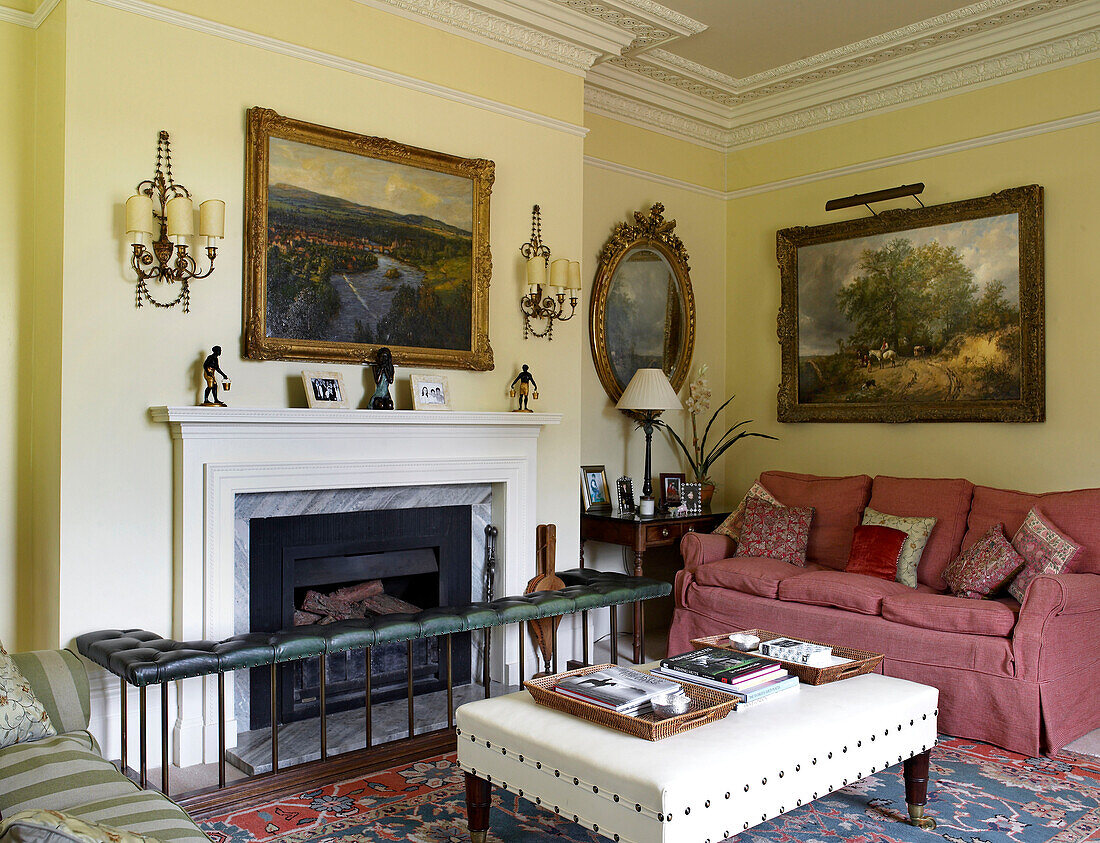 Umzäunter Sitz am Kamin im Wohnzimmer mit rosafarbenem Sofa in einem Landhaus in Lincolnshire, England, UK