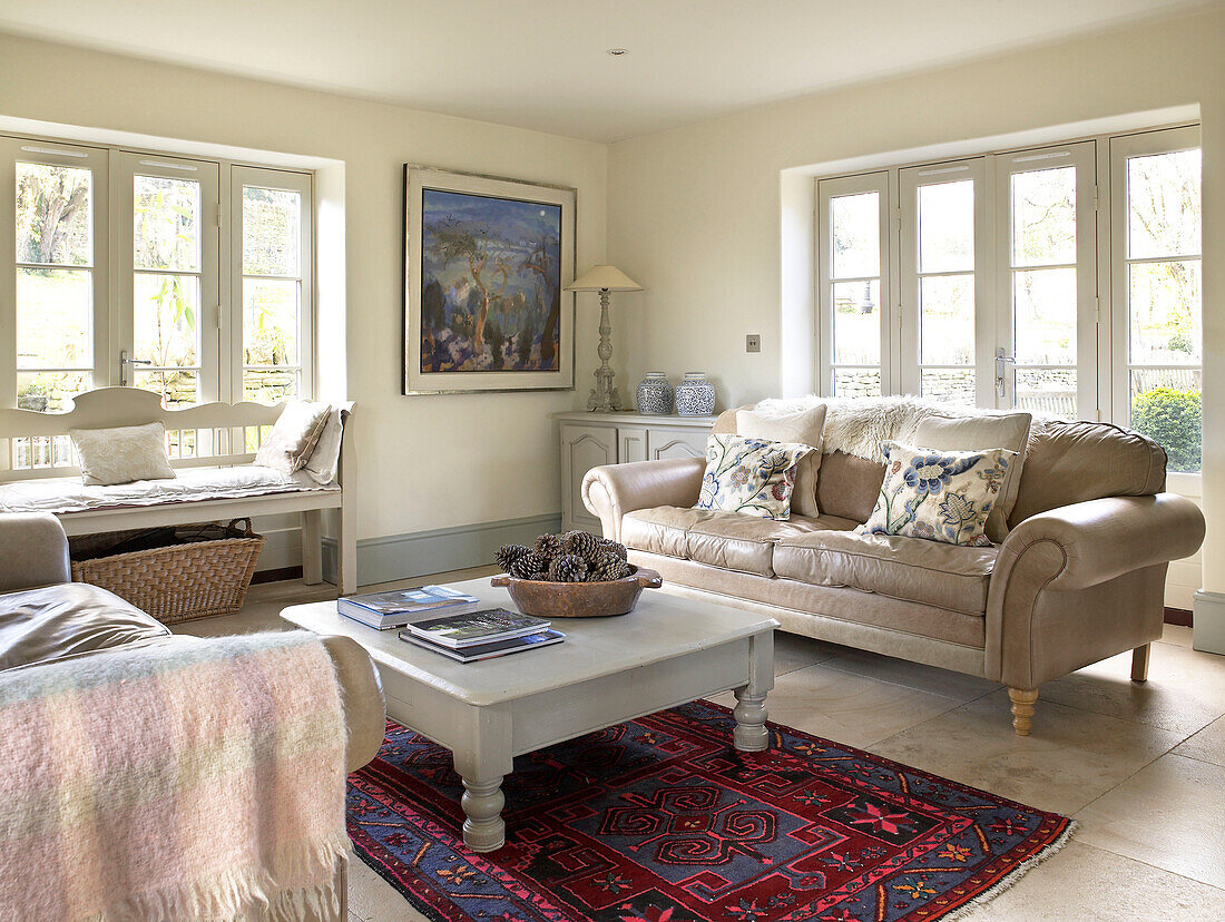 Leather sofa with painted coffee table on patterned rug in seating area of Gloucestershire farmhouse, England, UK