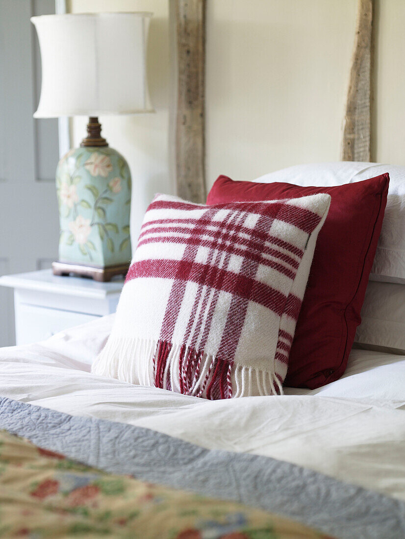 Rotes Tartan-Kissen auf einem Bett in einem Bauernhaus in Gloucestershire, England, UK