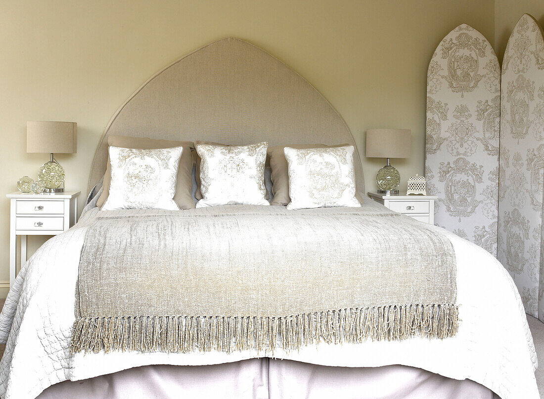 Folded blanket on bed with pointed arch headboard and co-ordinating cushions and folding screen Somerset new build rural England UK