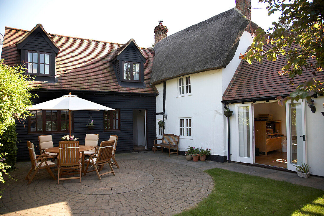 Tisch und Stühle mit Sonnenschirm im Innenhof eines weiß getünchten, strohgedeckten Cottages Buckinghamshire England UK