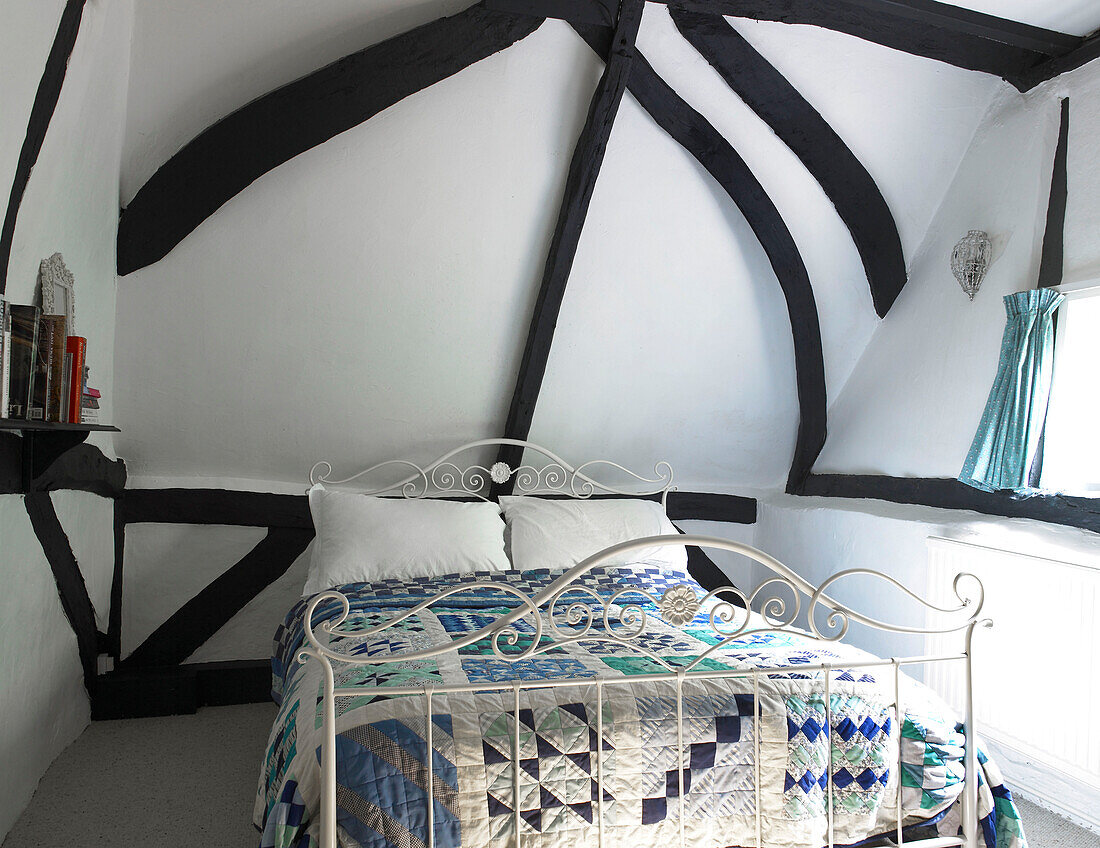 Patchwork quilt on metal bed in timber-framed bedroom of Buckinghamshire cottage England UK