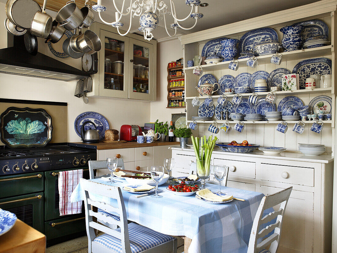 Decorative chinaware in kitchen dresser with set table and pan rack in Gloucestershire home, England, UK