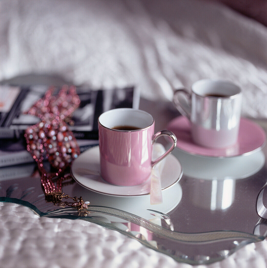 Tow pink coffee cups on a mirrored tray resting on top of a bed