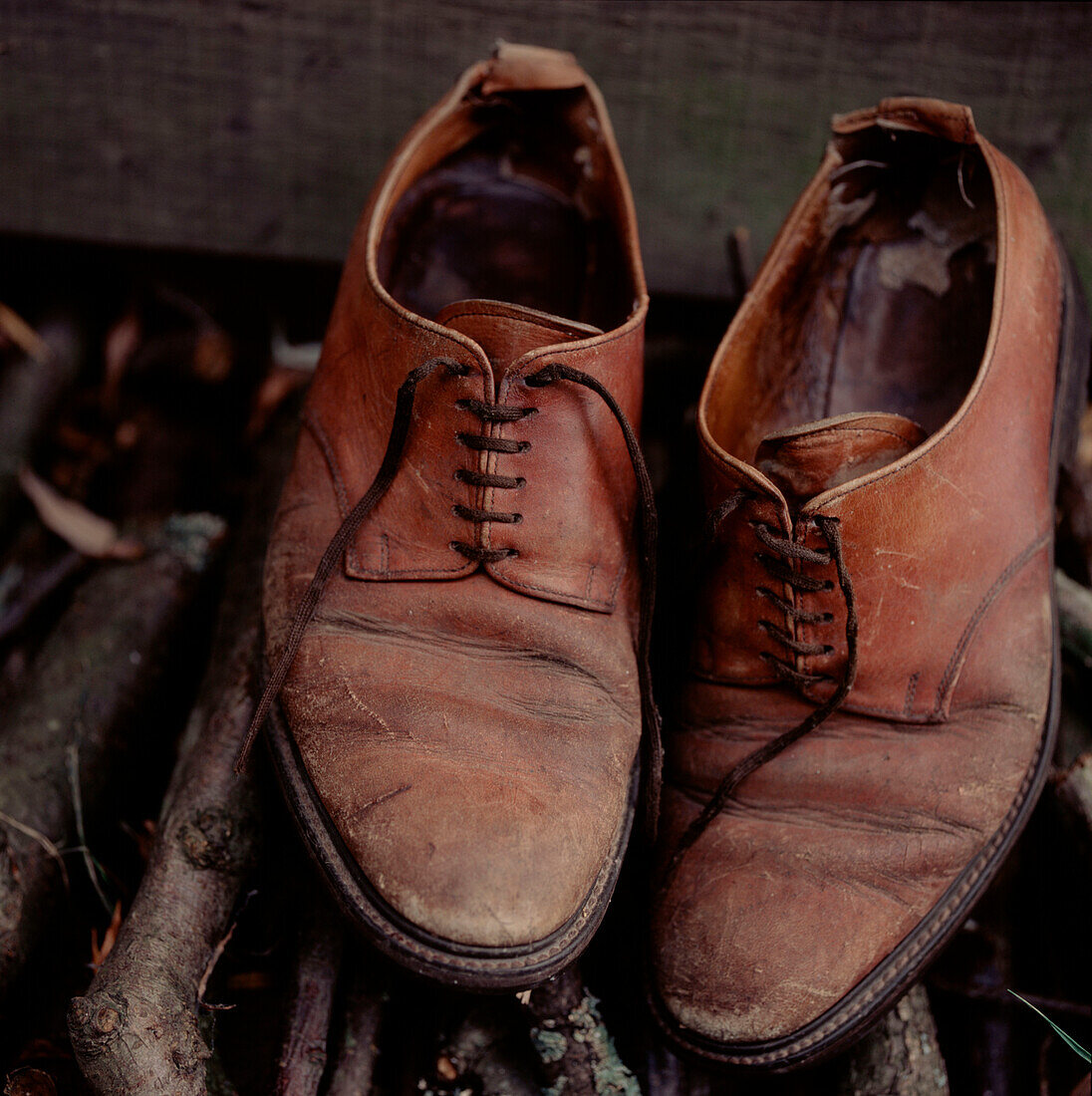 Ein Paar alte, abgenutzte braune Lederschuhe auf einem Holzstapel