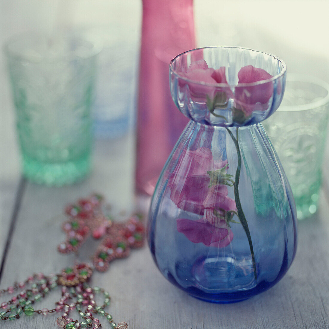 Coloured glassware on a wooden tabletop with a flower in a vase