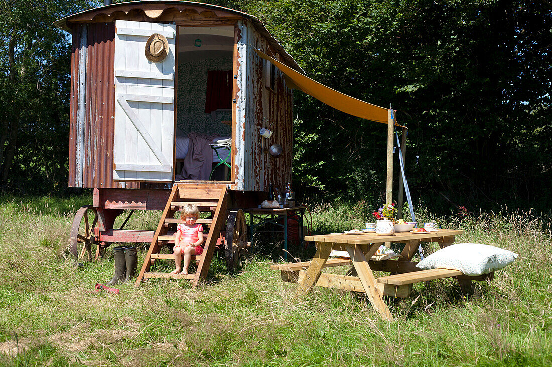 Little girl sitting on the step of a shepherds hut in a field