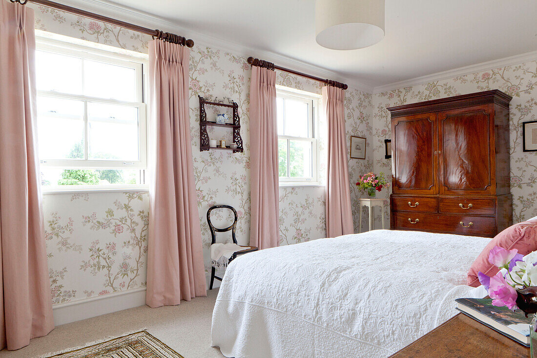 Rosa Vorhänge an Sprossenfenstern im Schlafzimmer mit poliertem antiken Holzschrank in einem Landhaus in Wiltshire England UK