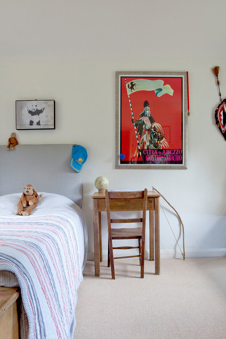 Red poster above wooden desk and chair beside single bed in Surrey cottage England UK