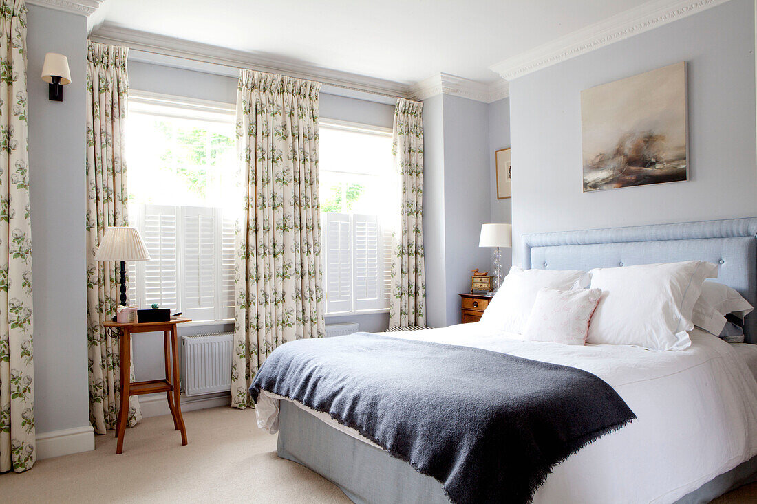 Dunkelgraue Decke auf einem Doppelbett in einem Zimmer mit floral gemusterten Vorhängen in einem modernen Haus in Chelsea, London, UK