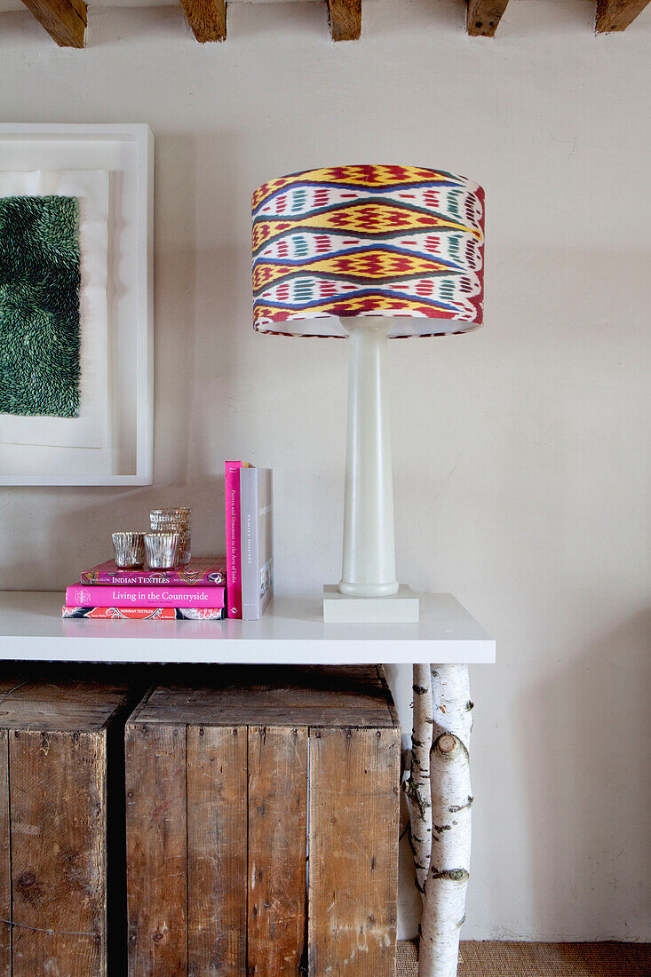 Wooden crates stacked under console made with tree branches with books and contemporary lamp