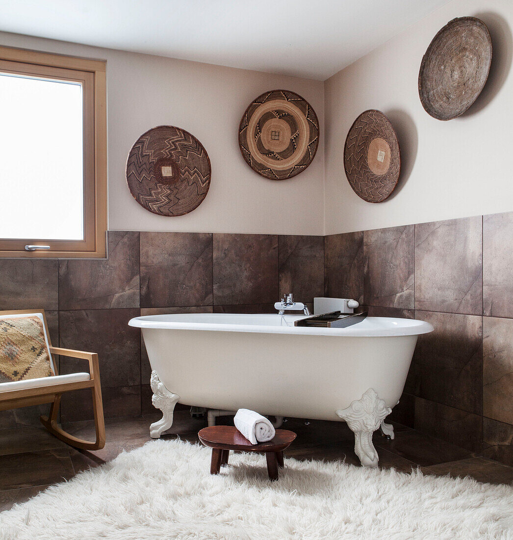 Freistehende Badewanne mit Schafsfellteppich und ethnischen Schalen in einem Haus in Lakes, England, Vereinigtes Königreich