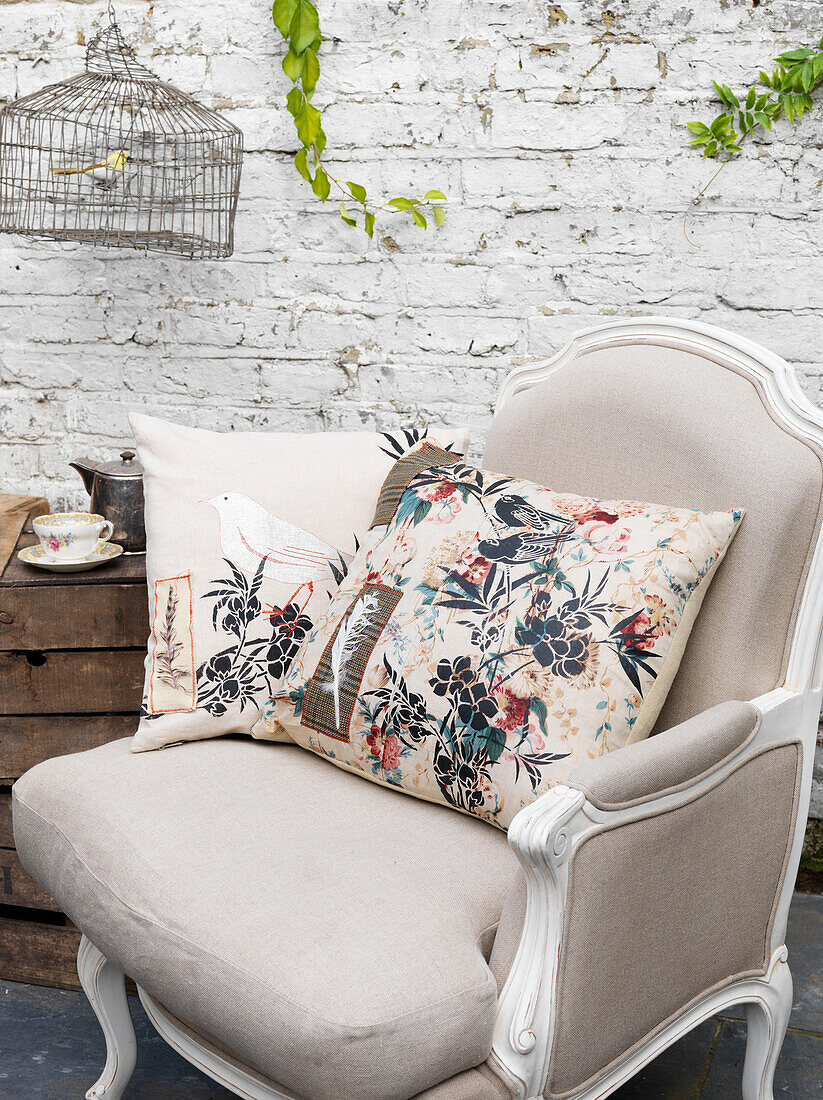 Floral cushion and birdcage with cream armchair in whitewashed room Battersea London UK