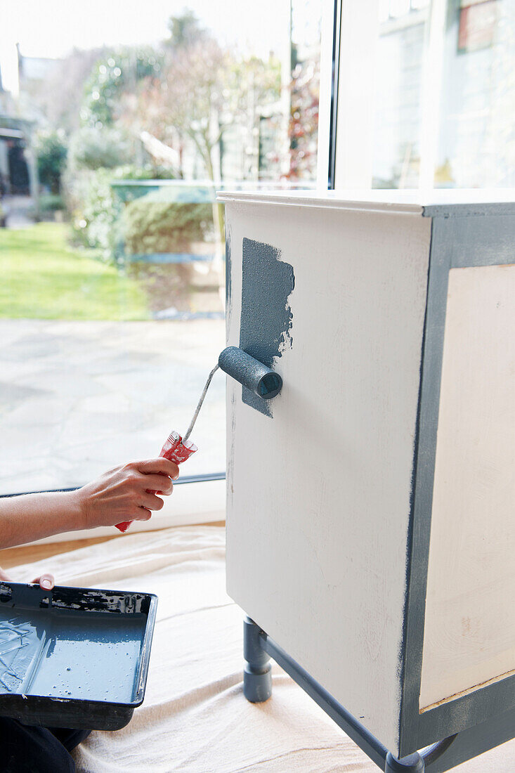 Person roller painting sideboard in UK home