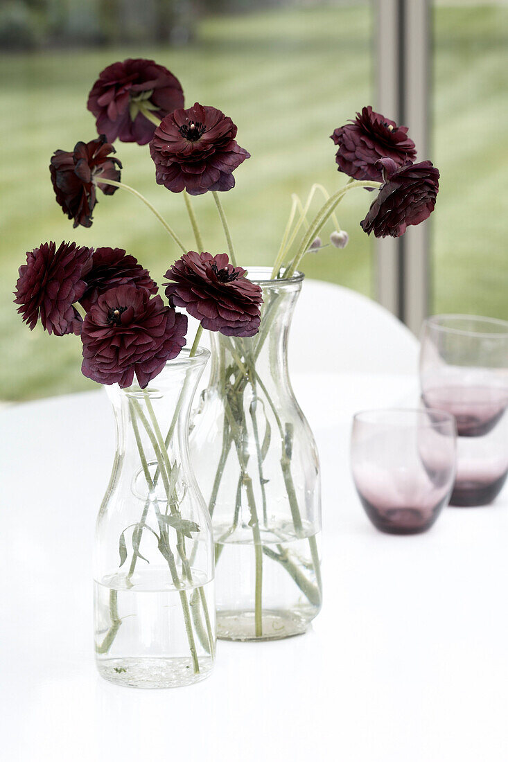 Two vases of flowers on a table with glasses