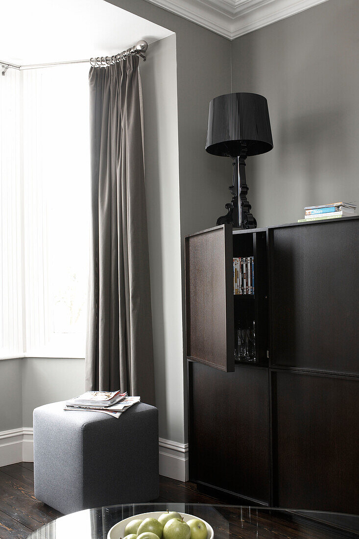 Dark wood storage unit at bay window of grey living room