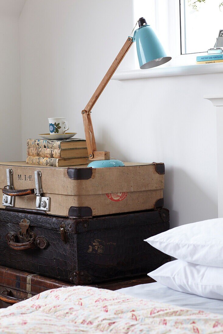 Schreibtischlampe auf einem Stapel Vintage-Koffer am Bett in einem Haus in Bembridge, Isle of Wight, UK