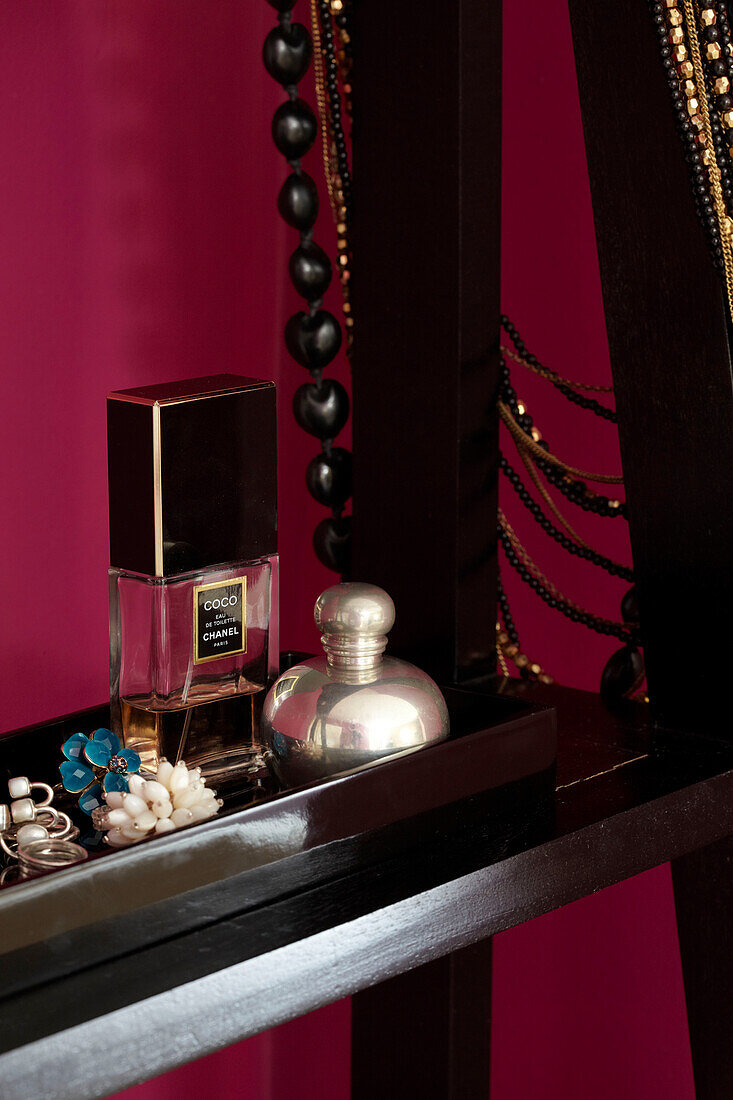 Perfume bottles and jewellery on black shelving unit in bedroom of London home England UK