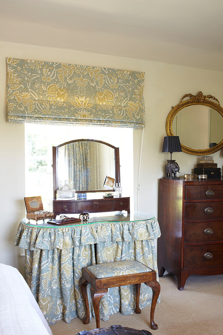 Oval gilt-framed mirror above wooden chest of drawers in Wiltshire bedroom with co-ordinating fabrics, England, UK