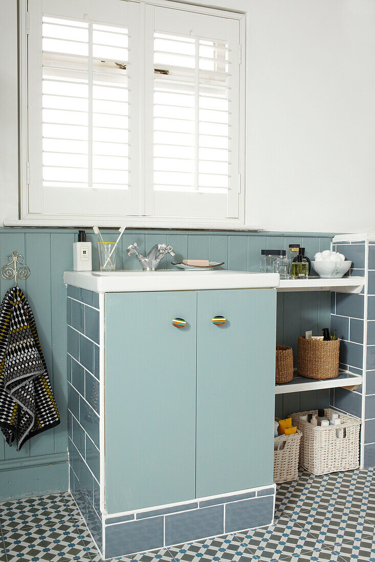 Light green wash stand with shelving below shuttered window in London bathroom, England, UK