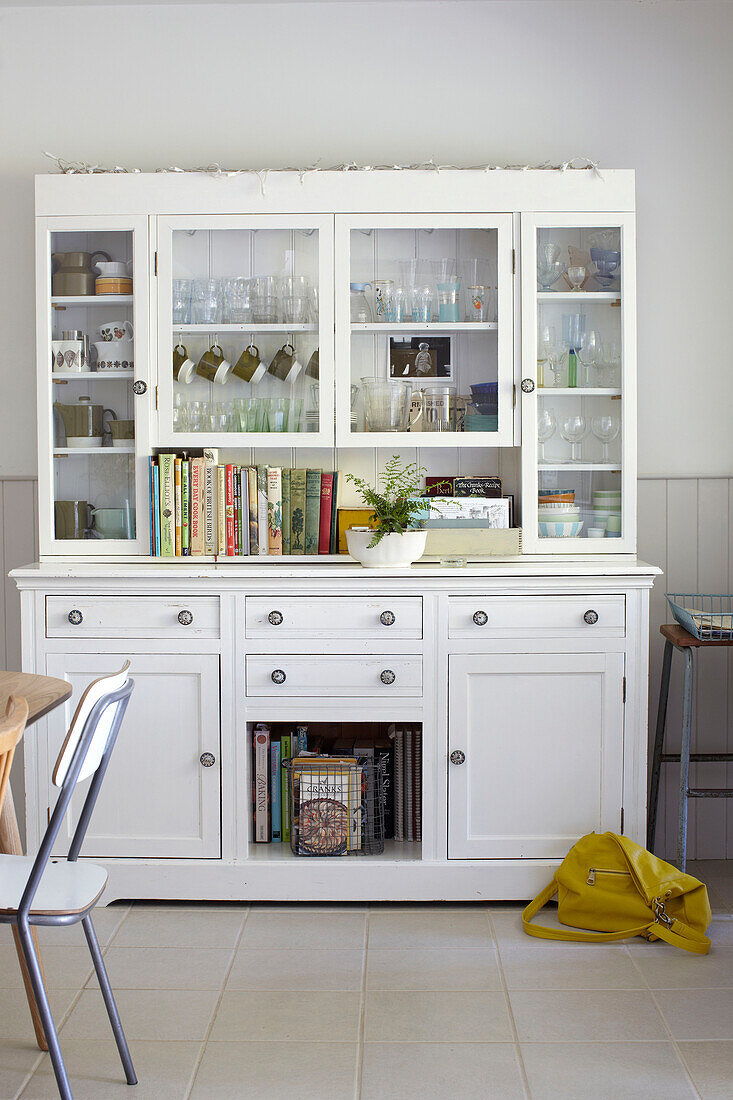 Recipe books and glassware on white kitchen dresser with yellow handbag in Ryde home Isle of Wight, UK