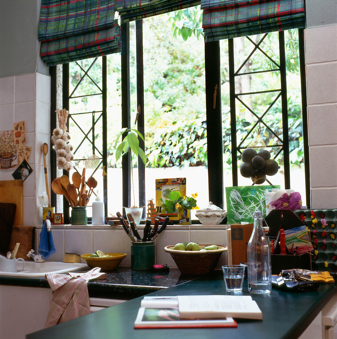 Nahaufnahme eines Küchenfensters mit bunt karierten Raffrollos und einer Arbeitsplatte mit Küchenutensilien