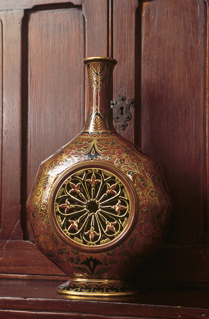 Nahaufnahme einer verschnörkelten Chinoiserie-Vase vor einer Holzvitrine