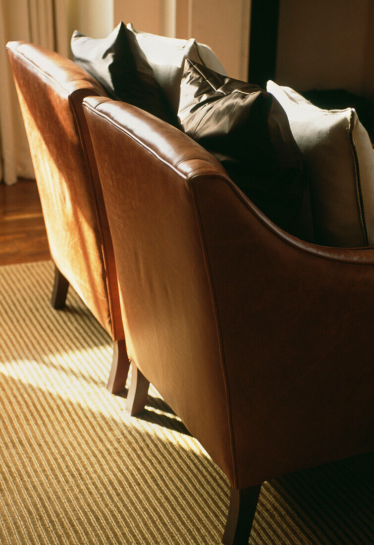 Detail of a pair of leather armchairs with silk and linen cushions on a striped rug