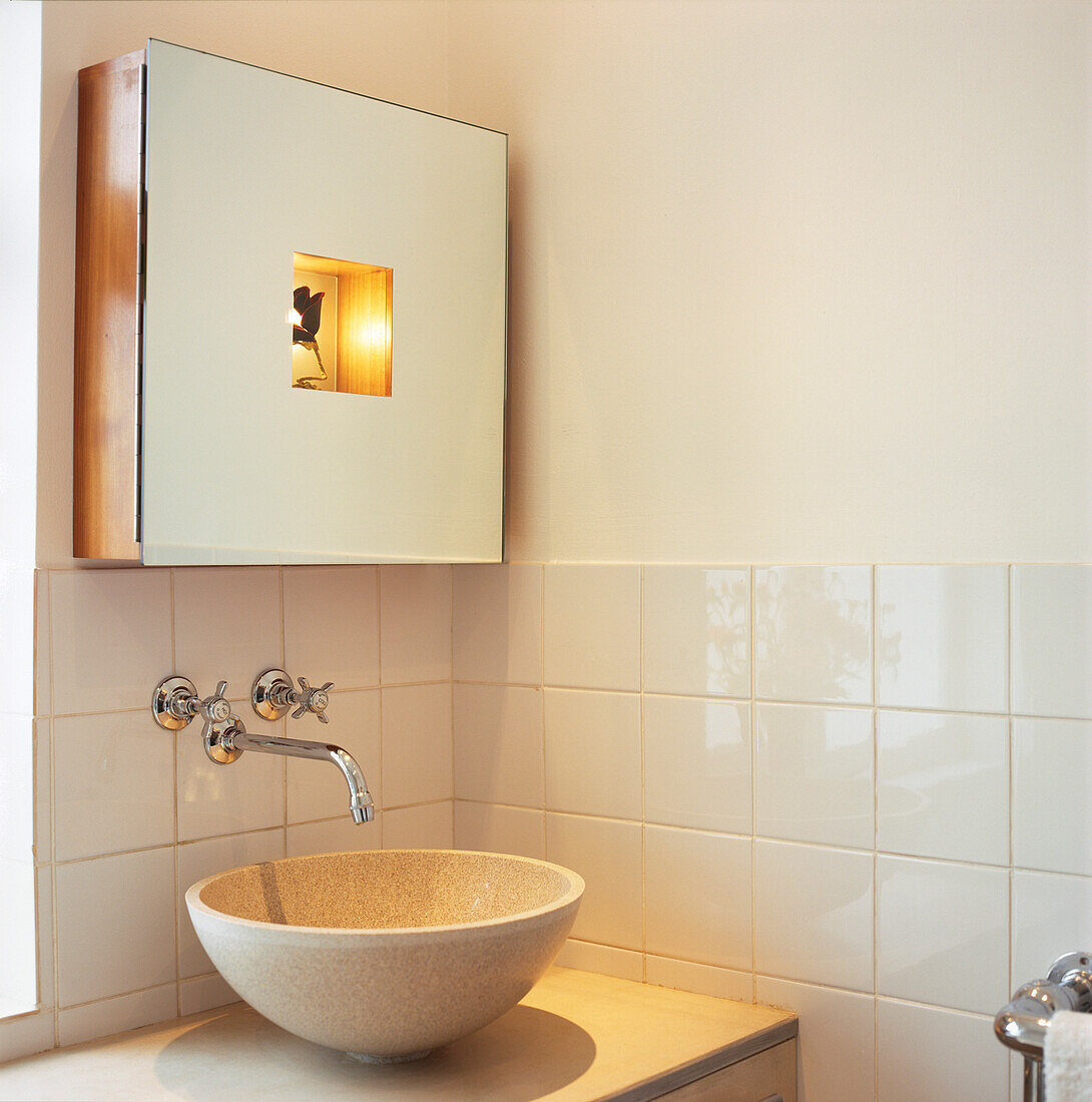 Eckdetail eines runden Handwaschbeckens aus Stein und Spiegelschrank mit integrierter Beleuchtung