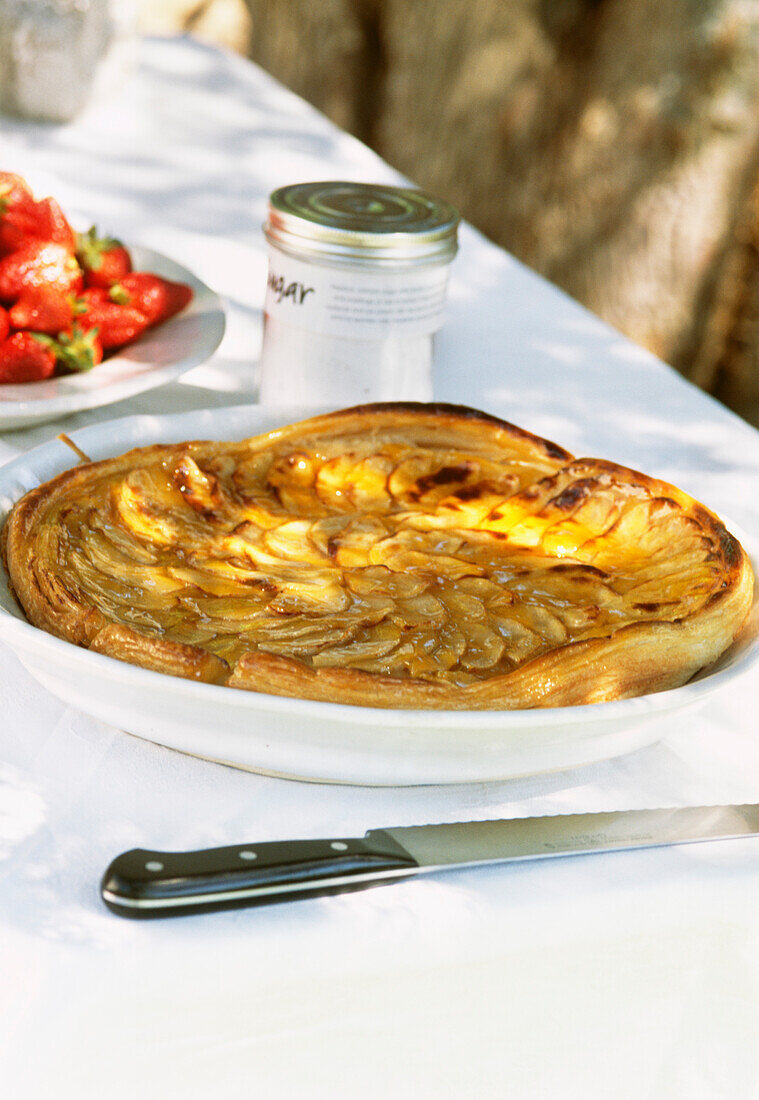 Homemade French apple tart on garden table with knife and white table linen