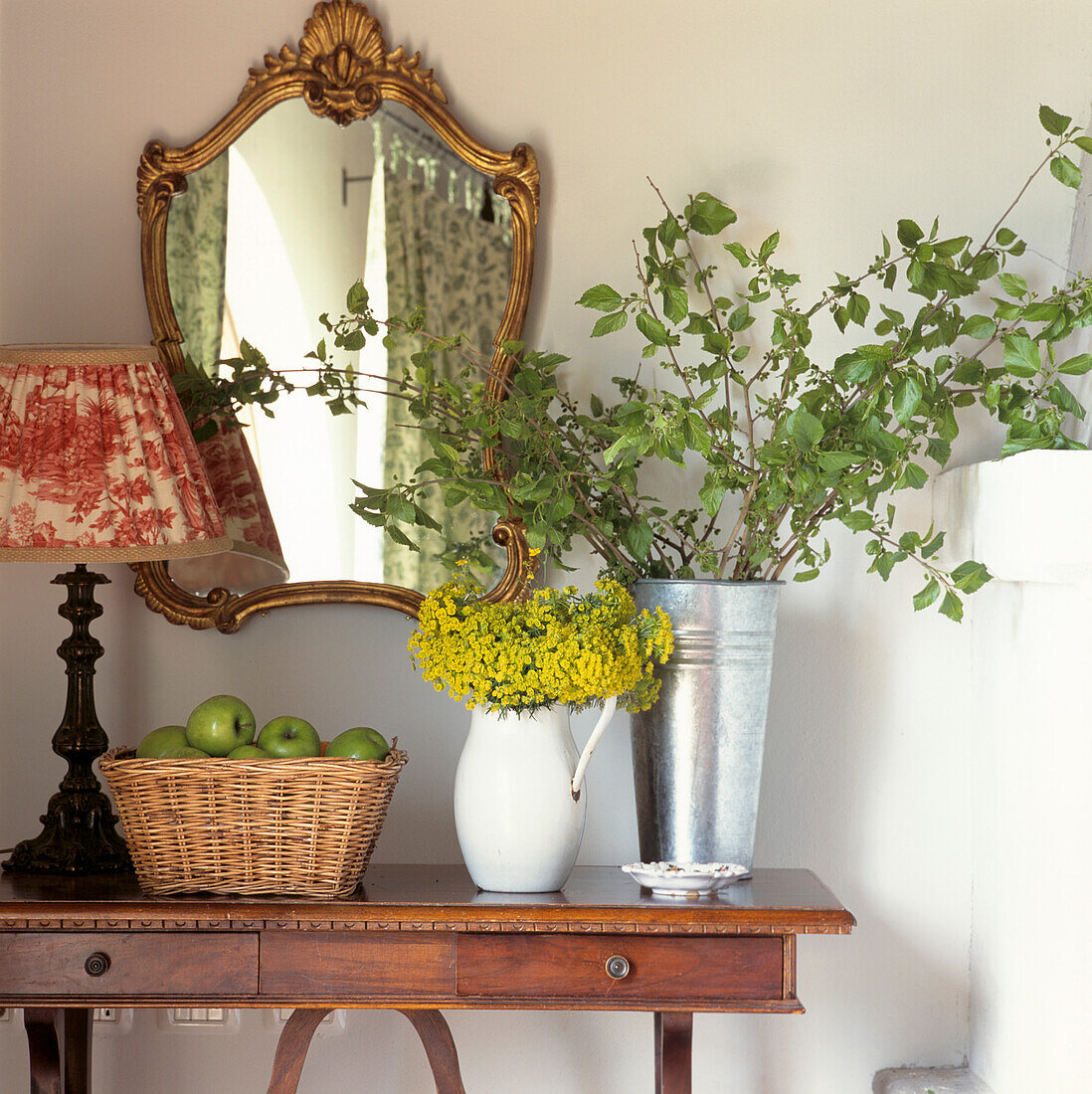 Flurtisch mit vergoldetem Spiegel, Korb mit Äpfeln und saisonalem Blumenarrangement