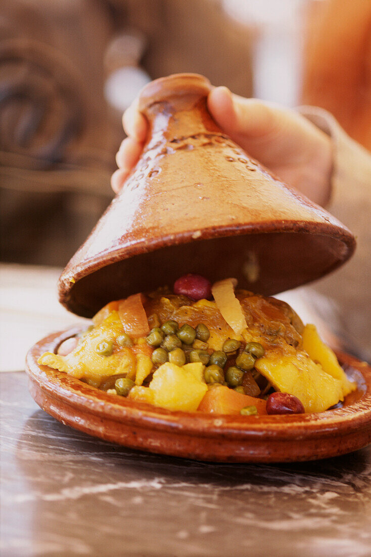 Öffnen eines frisch gekochten Tajine-Topfes mit gesundem Essen in der Medina von Fez, Marokko