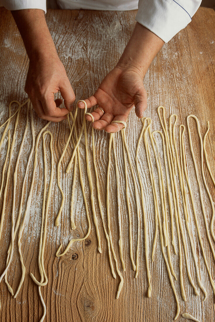 Chefs hands preparing freshly made noodles on a floured kitchen worktop