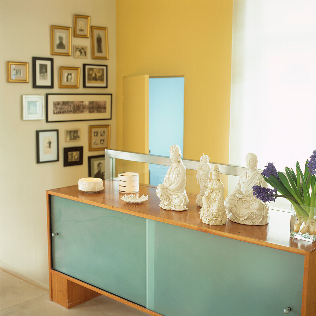 Blanc de Chine Buddha on modern sideboard in front of the stairwell lined with family portraits