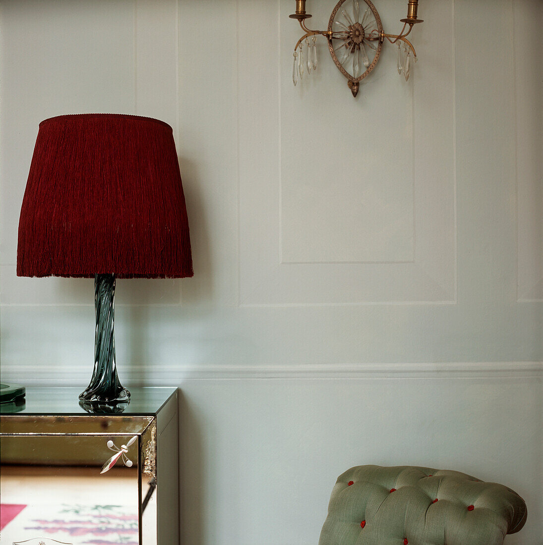 Faux panelled walls in soft blue with wall light and purple fringed lampshade on a green glass base sitting on top of a mirrored sideboard