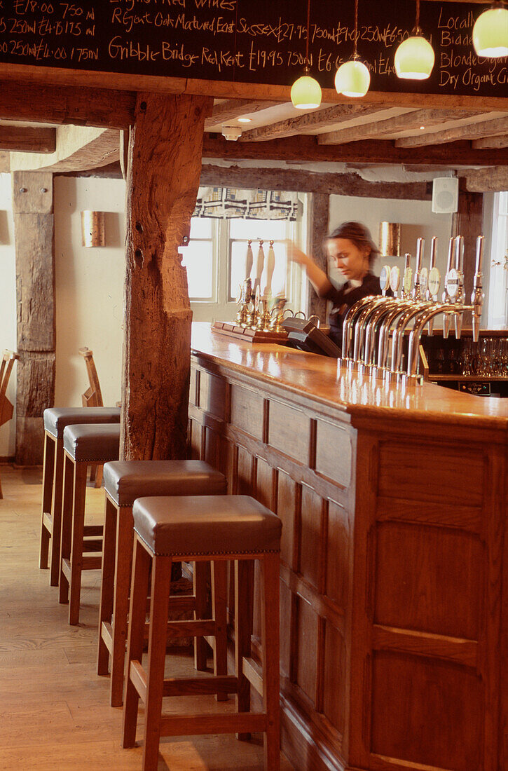 Young woman pulling a pint behind the bar of a traditional public house 